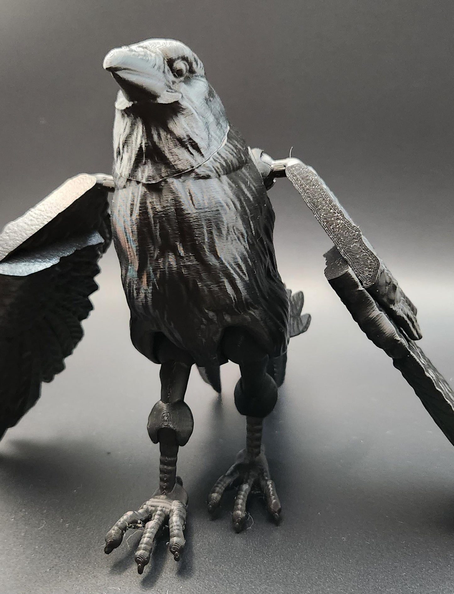 Black articulated raven figurine with detailed feathers and movable wings standing on a black surface
