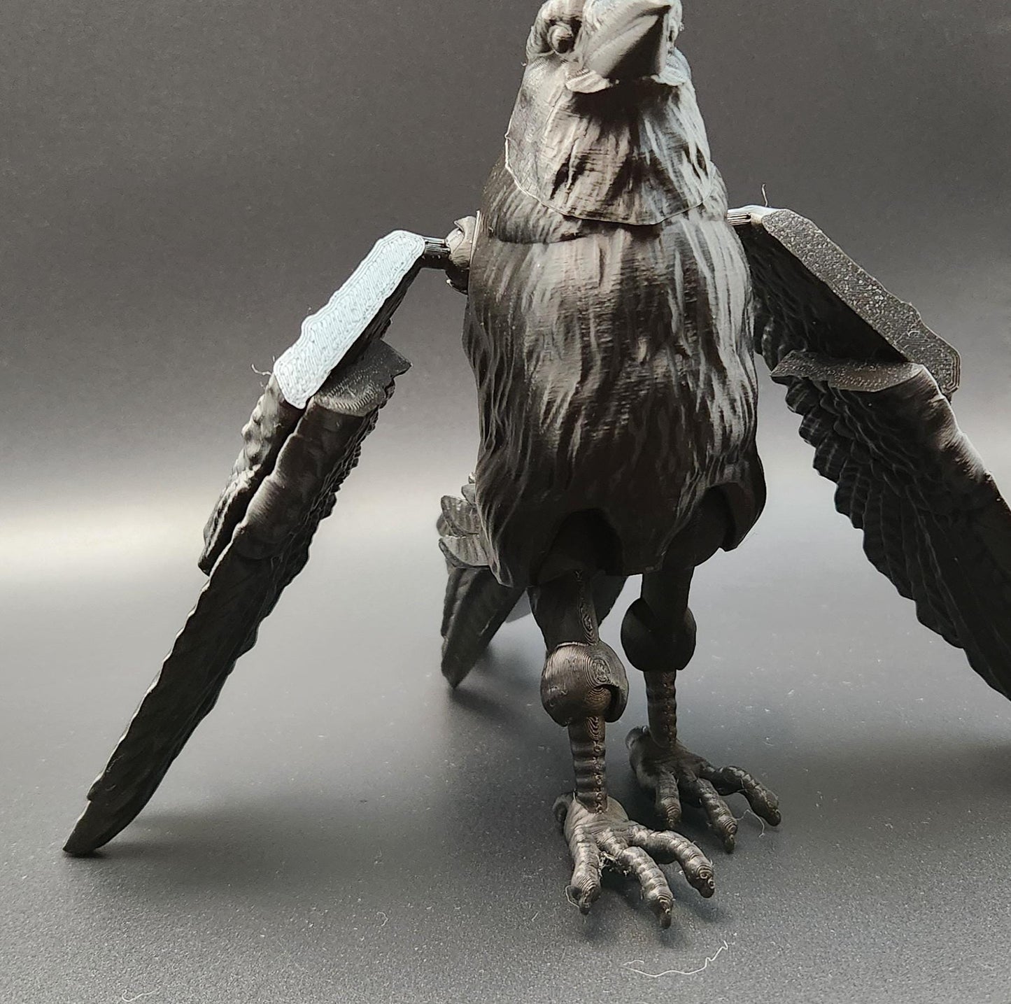 Black articulated raven figurine with detailed feathers and movable wings on a gray surface
