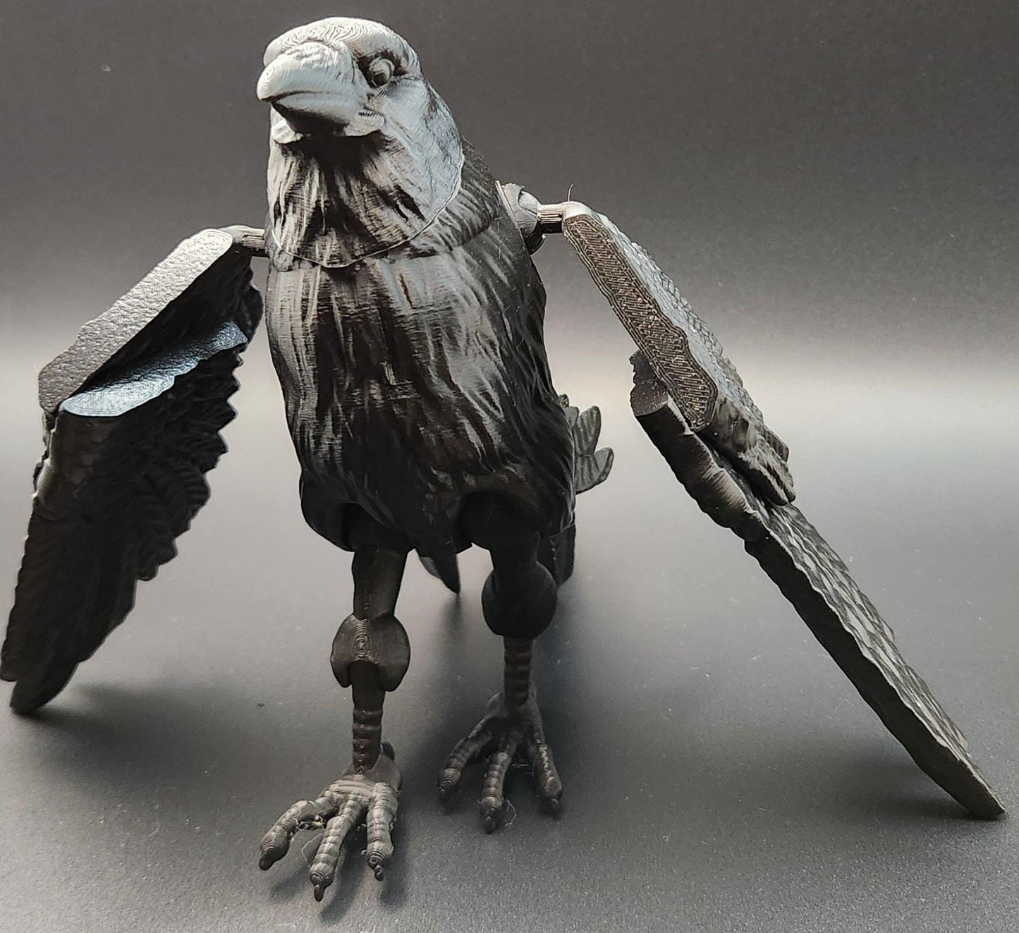 Black articulated raven figurine with detailed feathers and movable wings on a gray background
