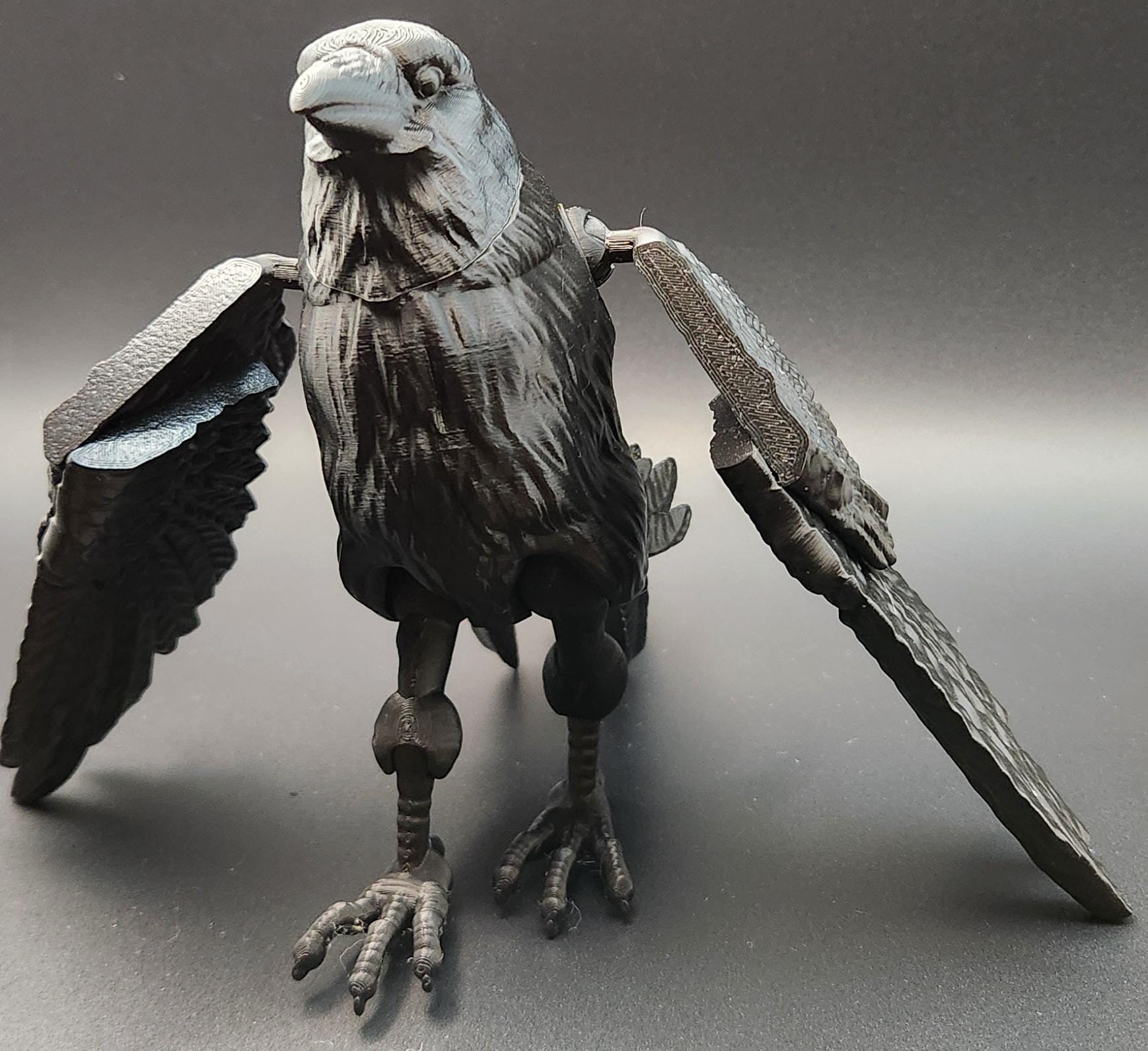 Black articulated raven figurine with detailed feathers and movable wings on a gray background