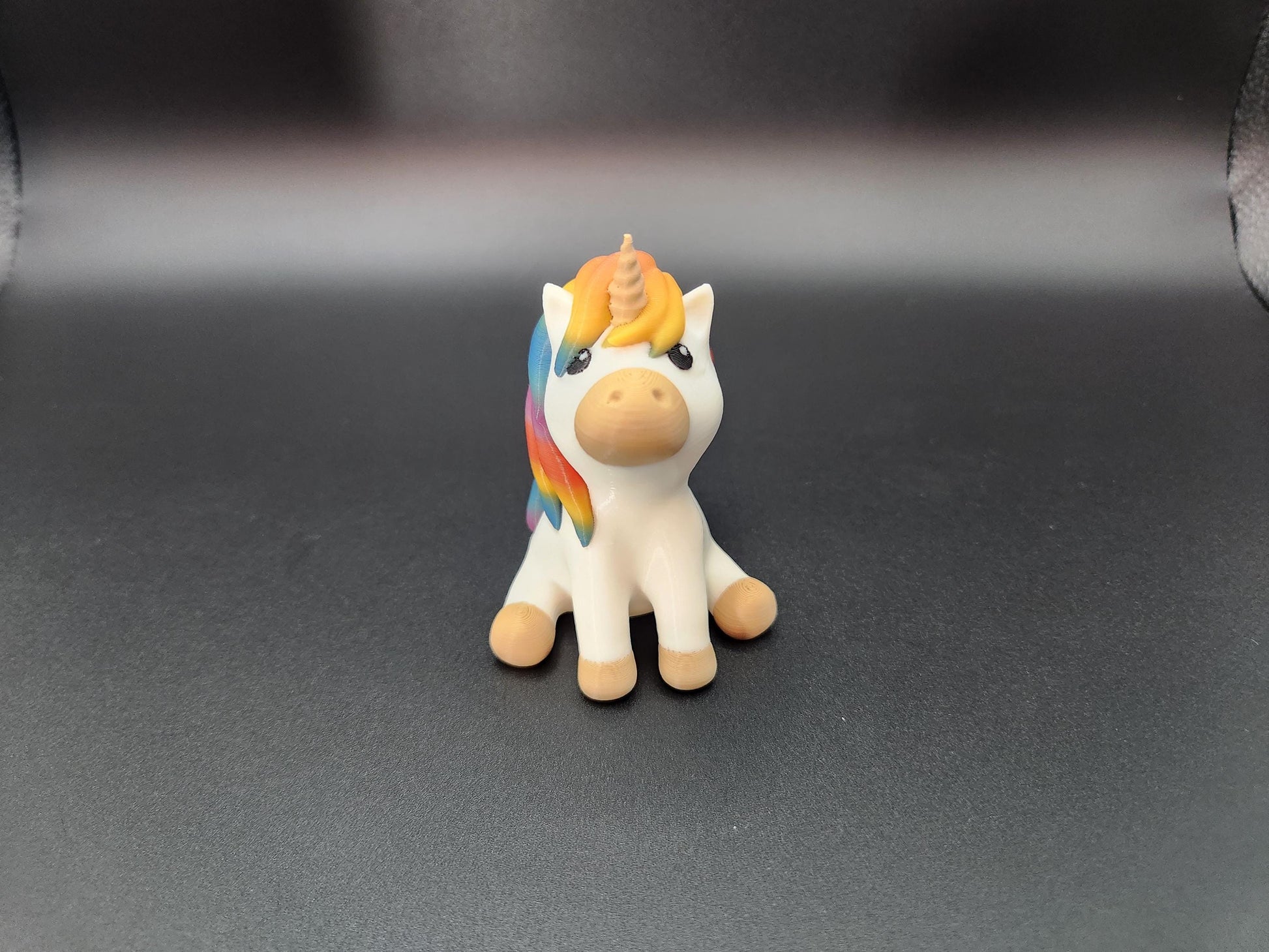 Cute rainbow unicorn keychain with bright multicolor mane and tail sitting against black background
