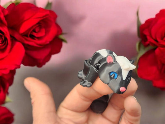 Hand holding a realistic articulated Skunk Fidget toy with black and white details among red roses