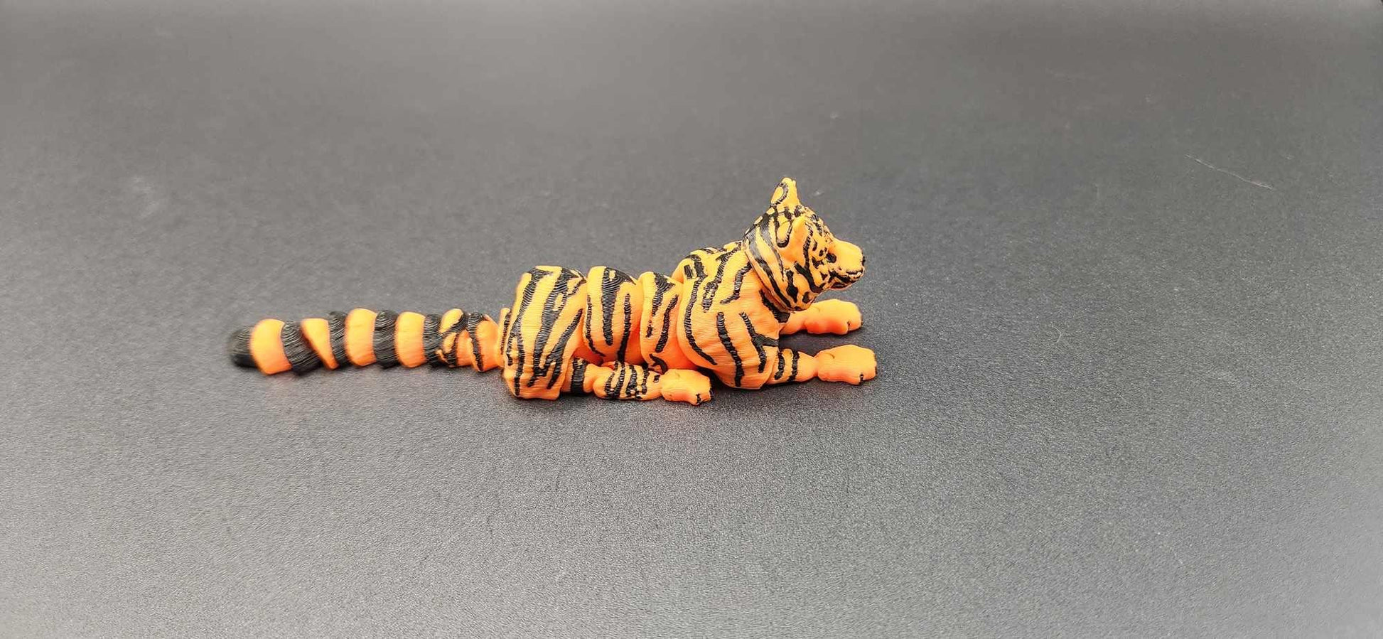 Realistic tiger figurine 3D print in orange and black stripes lying down on gray surface