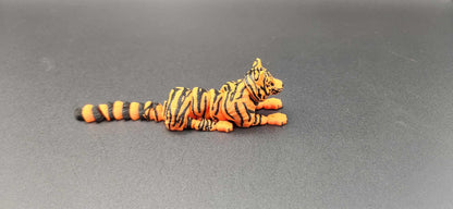 Realistic tiger figurine 3D print in orange and black stripes lying down on gray surface