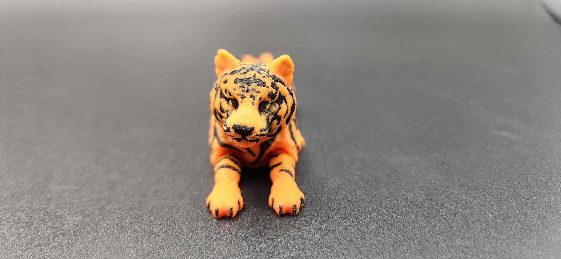 Realistic tiger figurine 3D print in orange and black lying down on a gray surface