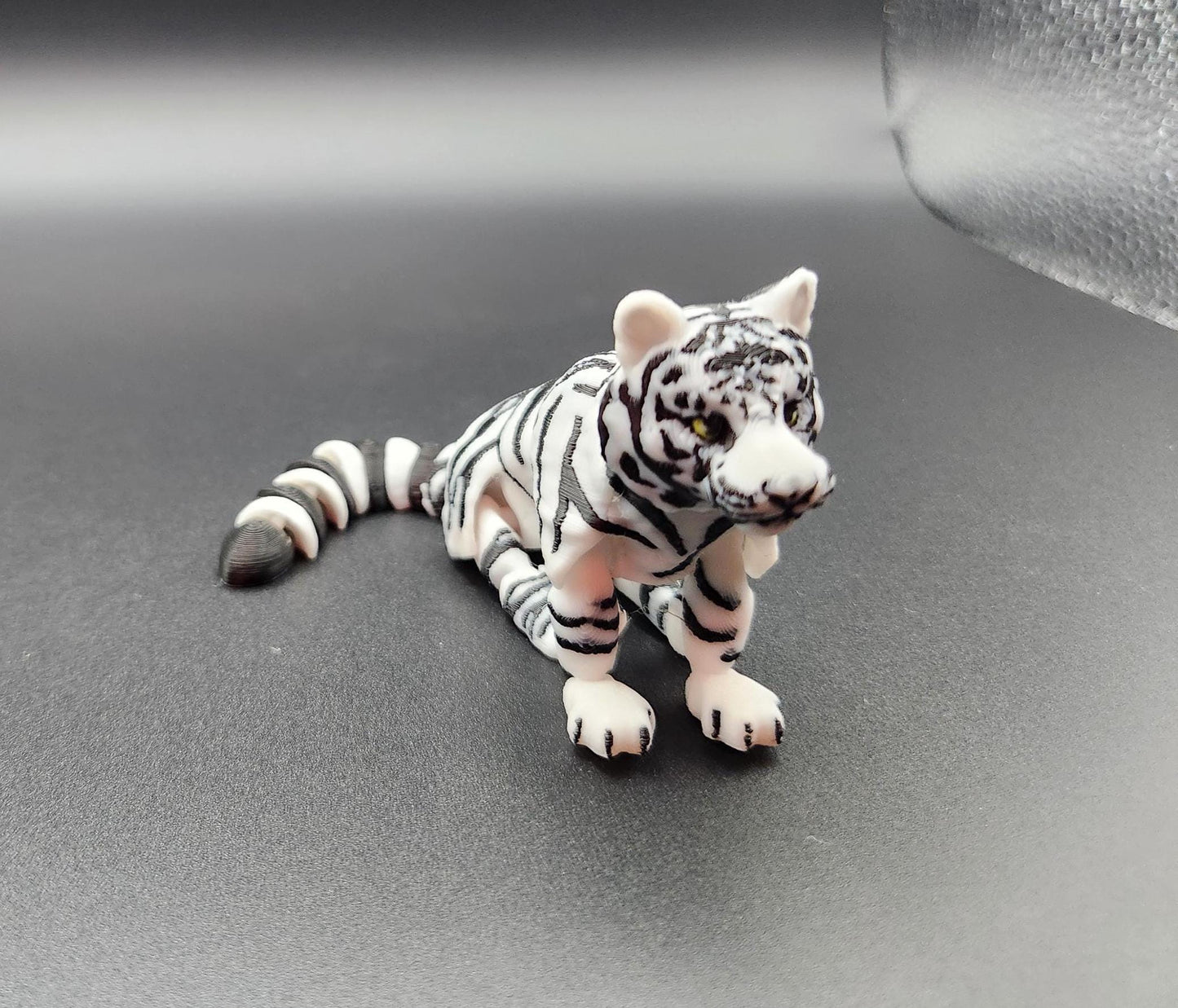 Realistic tiger figurine 3D print in white and black stripes lying on a dark surface