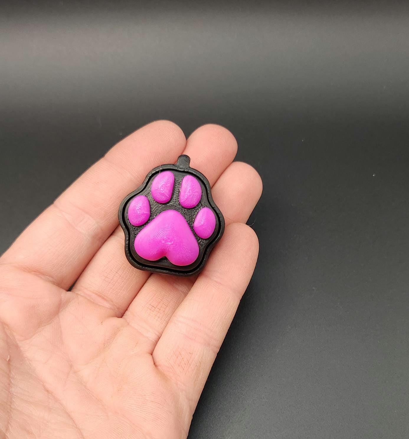  a pink and black paw-shaped sensory stress relief clicker on a black background