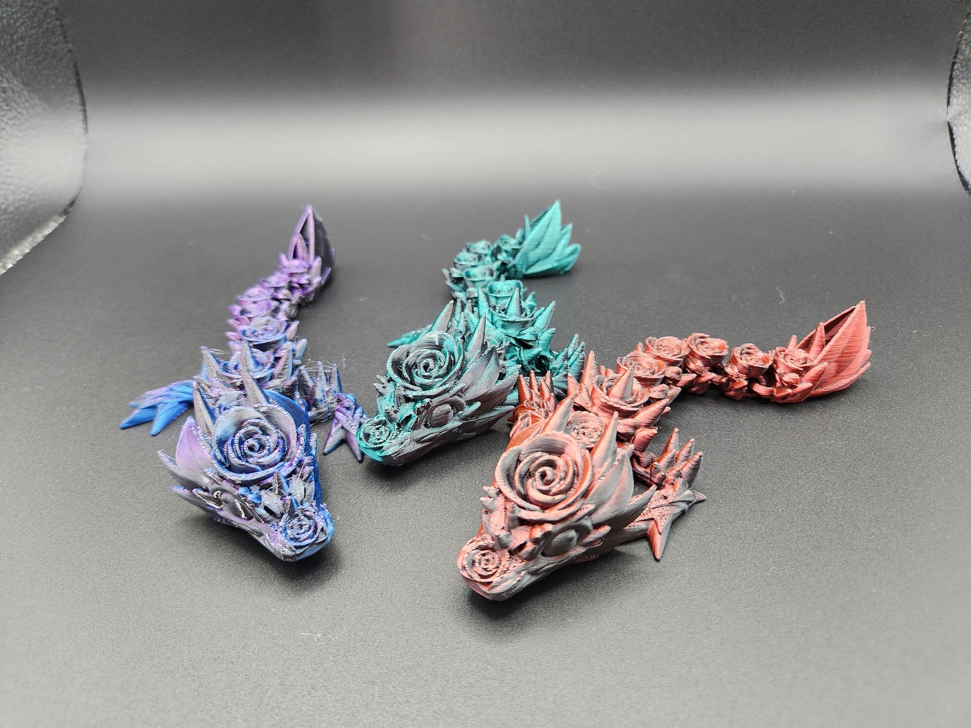 Three colorful 3D printed baby dragon figurines in purple, green, and red with detailed floral and spiked designs