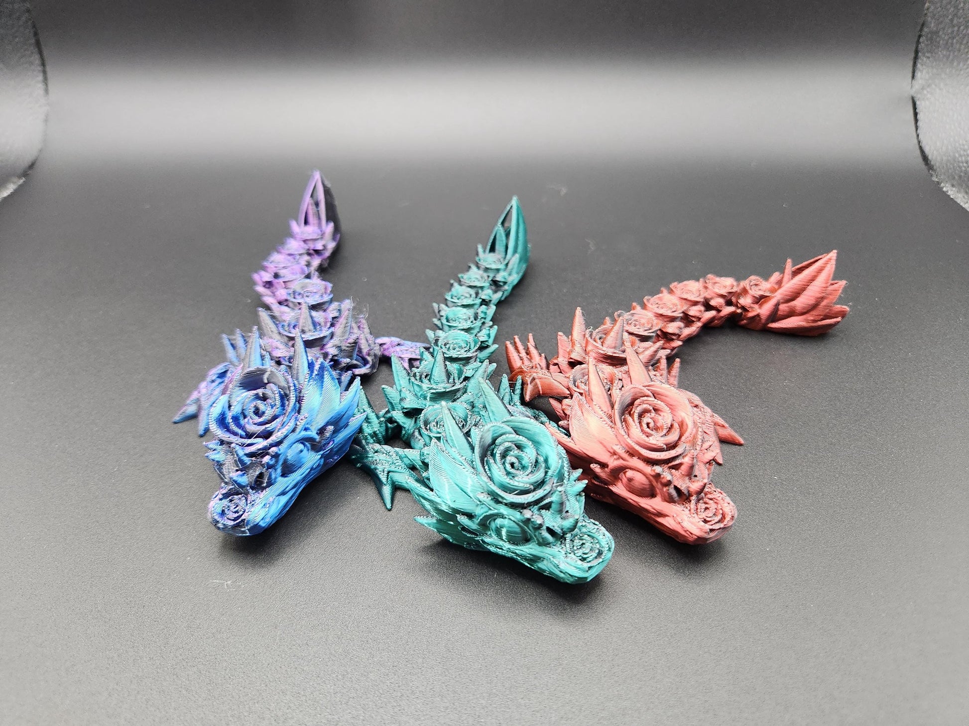 Set of three colorful 3D printed baby dragon figures in blue, teal, and pink with intricate floral details