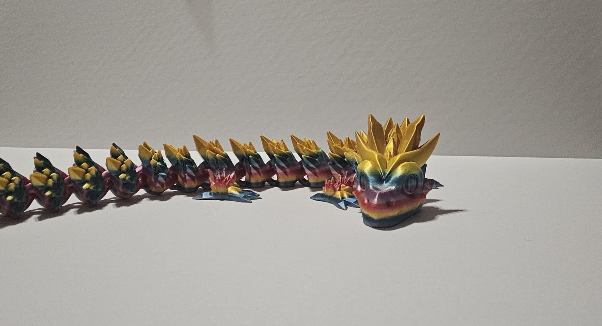 Colorful 3D printed crystal dragon figurine with yellow spiked head and segmented body on white surface