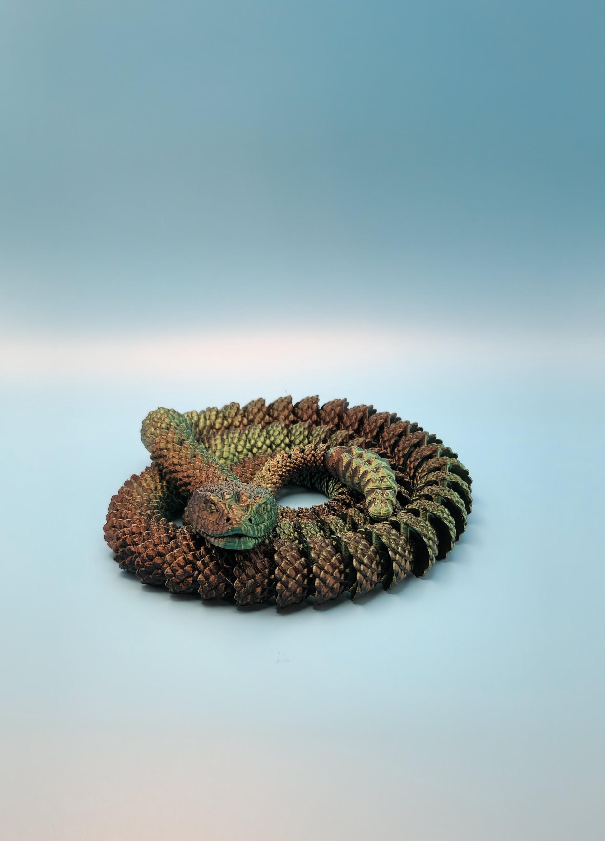 Detailed 3D printed rattlesnake toy coiled on a blue surface with textured scales and realistic colors