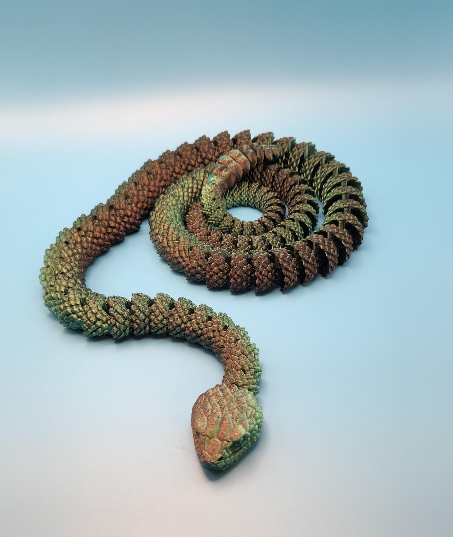 Green and brown detailed 3D printed rattlesnake toy coiled on a light blue surface