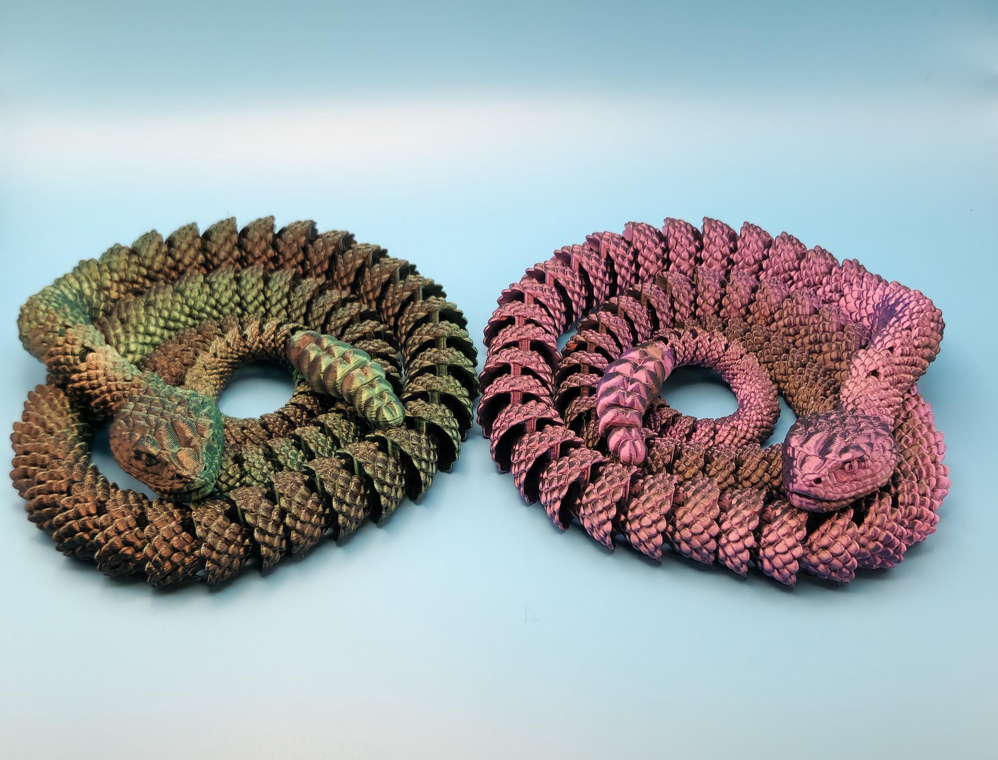 Green and pink 3D printed rattlesnake toy pairs, detailed coiled snake figures on light background