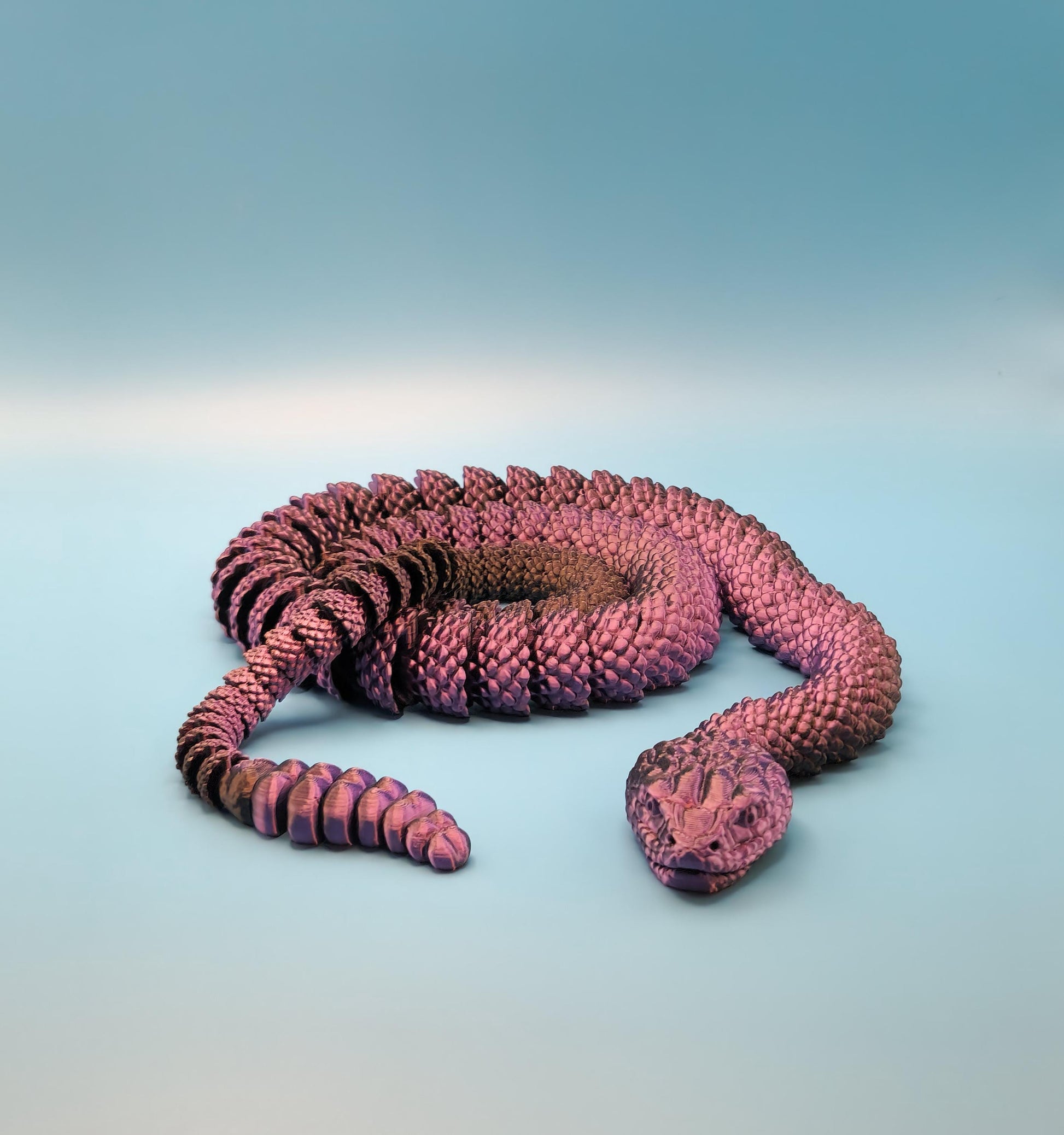 Purple 3D printed rattlesnake toy with detailed scales coiled on a blue surface