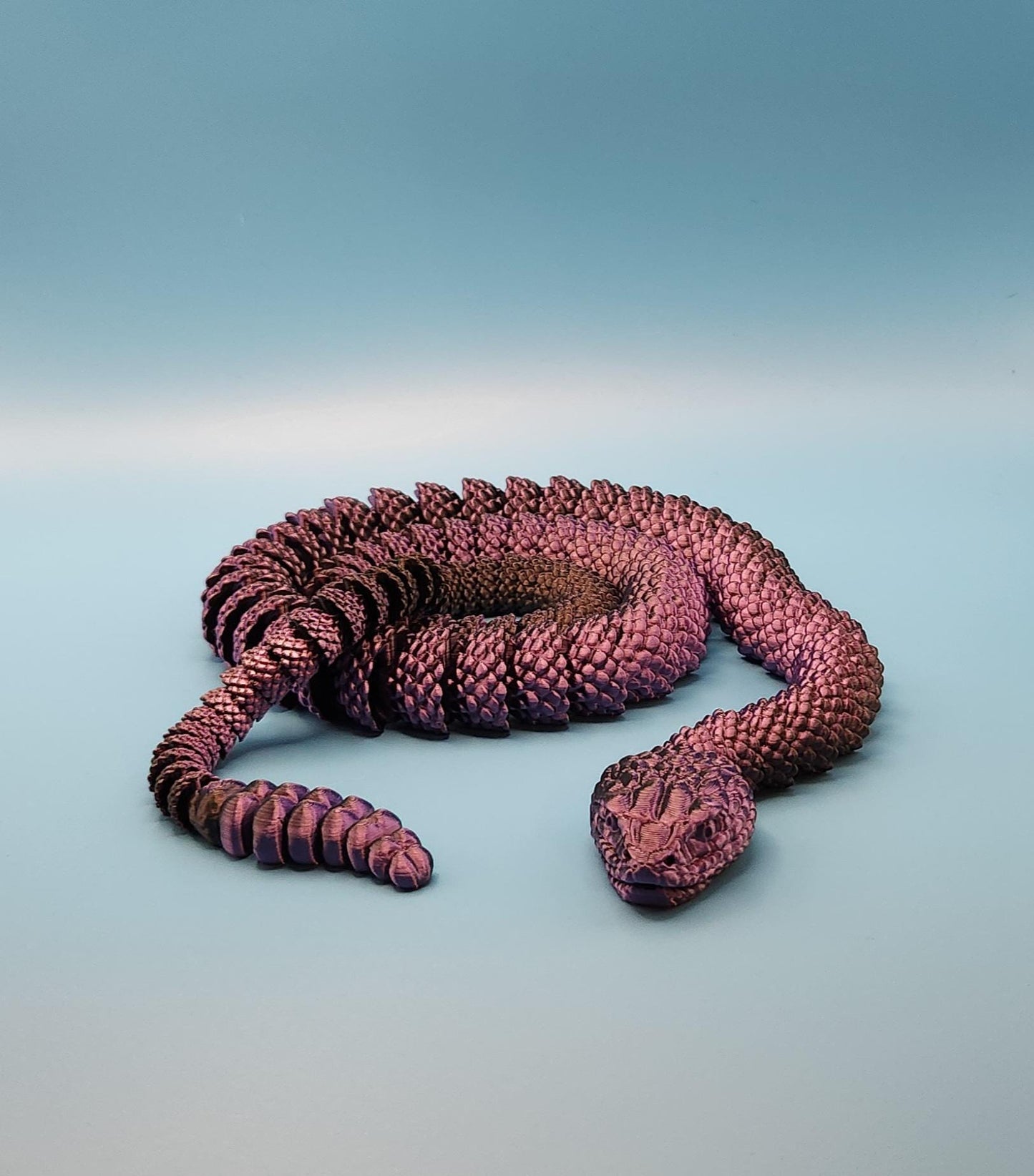 Purple 3D printed rattlesnake toy with detailed scales coiled on a light blue background