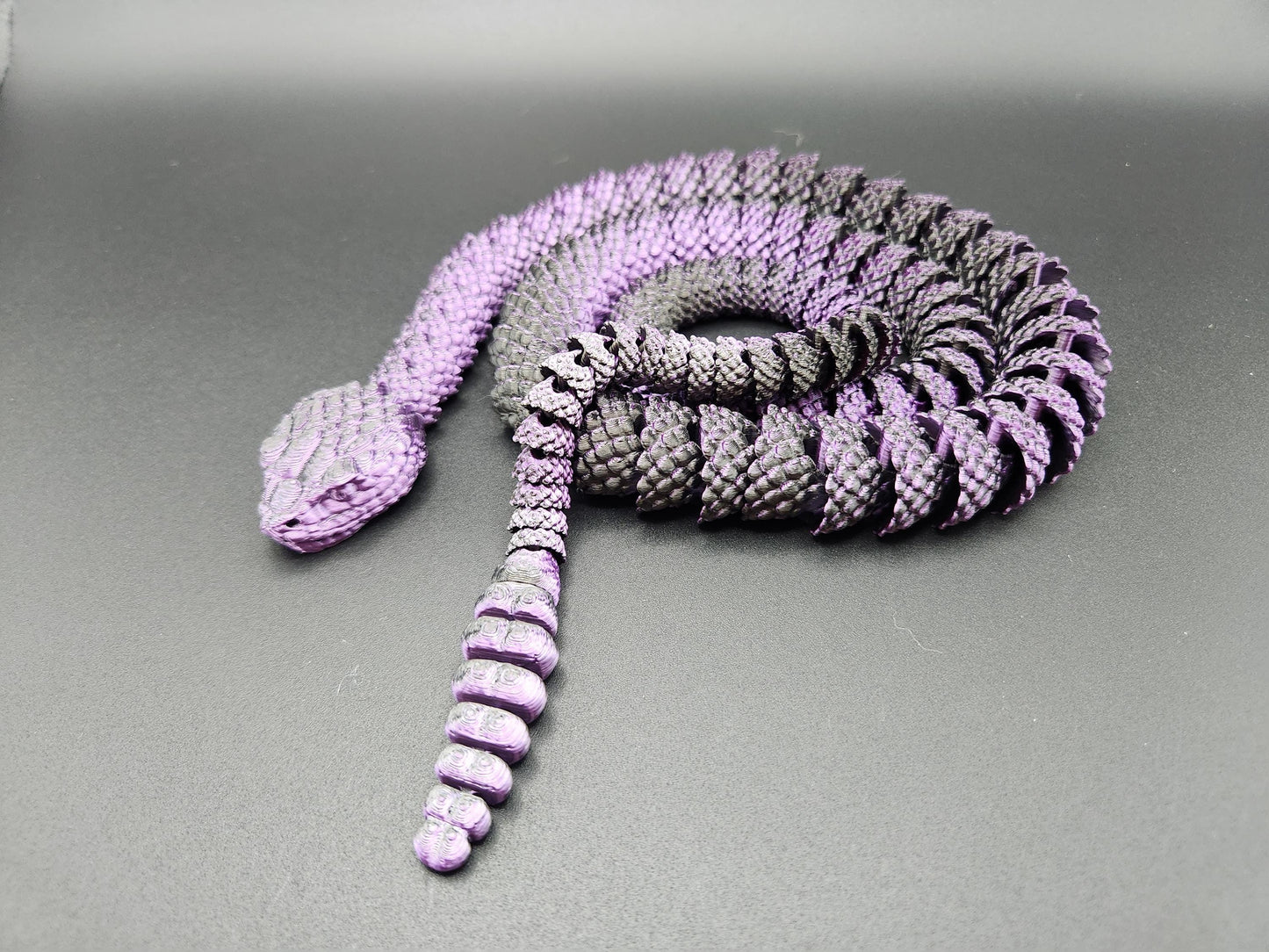 Purple and black 3D printed rattlesnake toy displayed on a dark surface with detailed segmented body