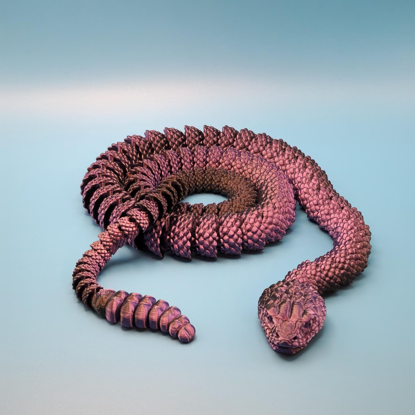 Purple and black 3D printed rattlesnake toy coiled on a light blue background
