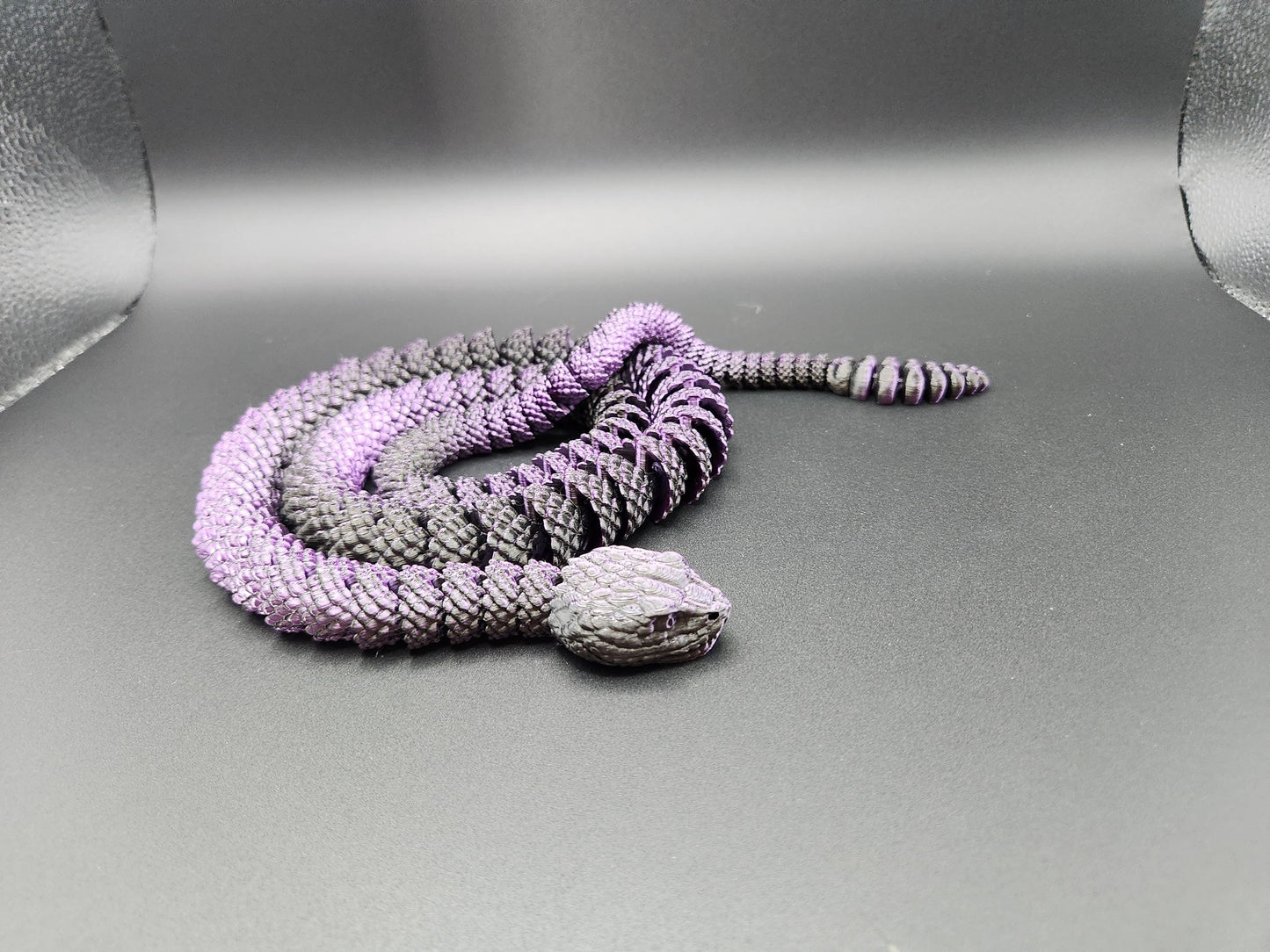 Close-up of a purple and black 3D printed rattlesnake toy displayed on a gray surface