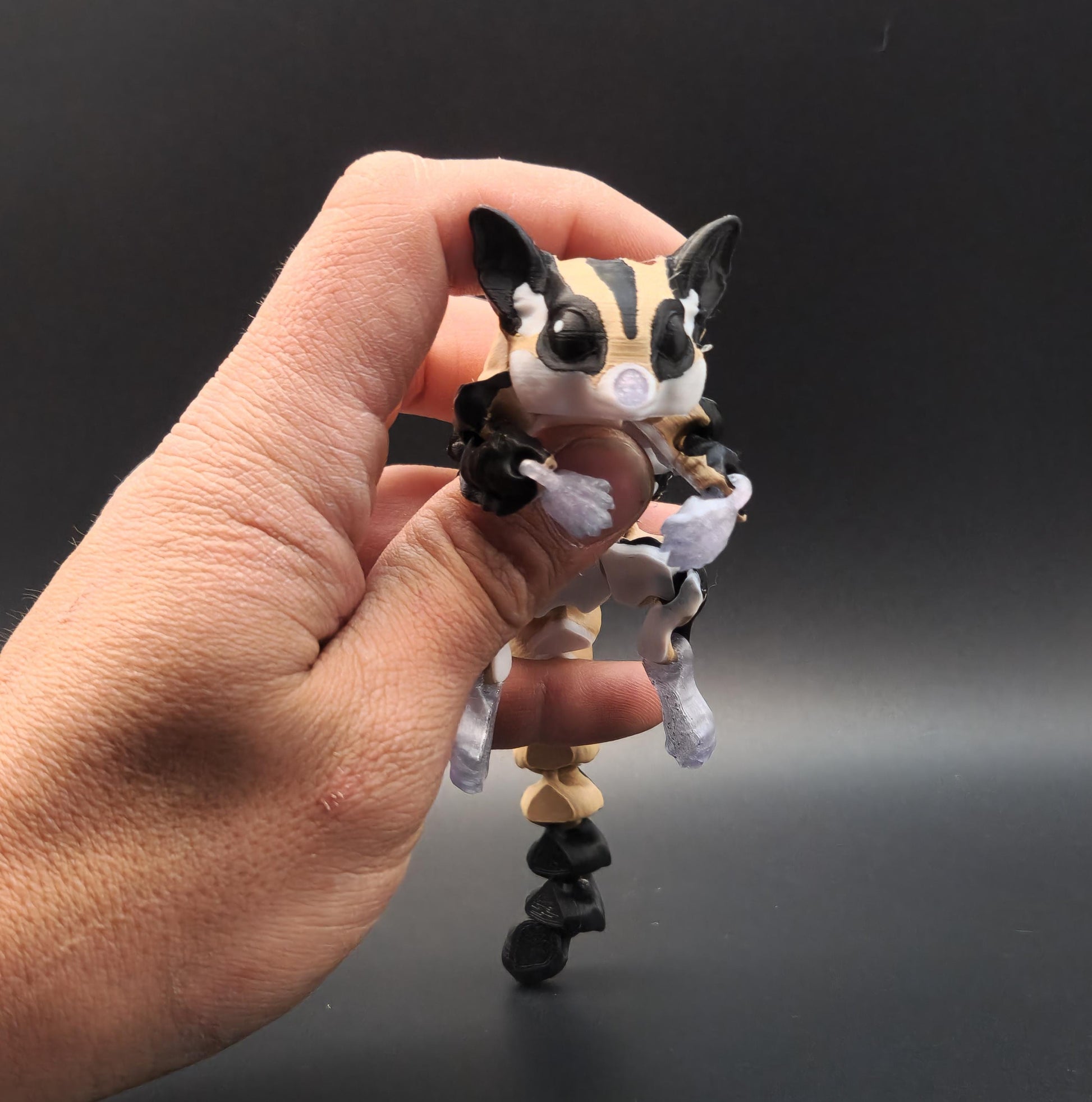 Hand holding a detailed 3D printed sugar glider figurine with black and beige coloring