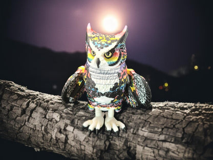 Poseable articulated rainbow great horned owl figurine perched on a tree branch at night