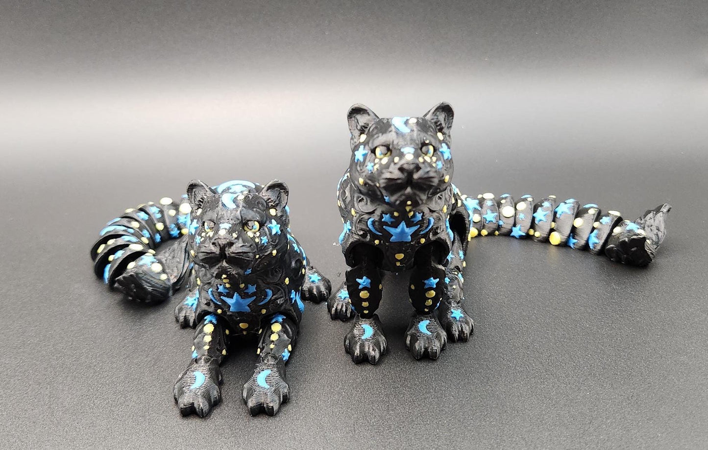 Black star and moon fidget panther figurines with blue and yellow celestial designs on shiny surface