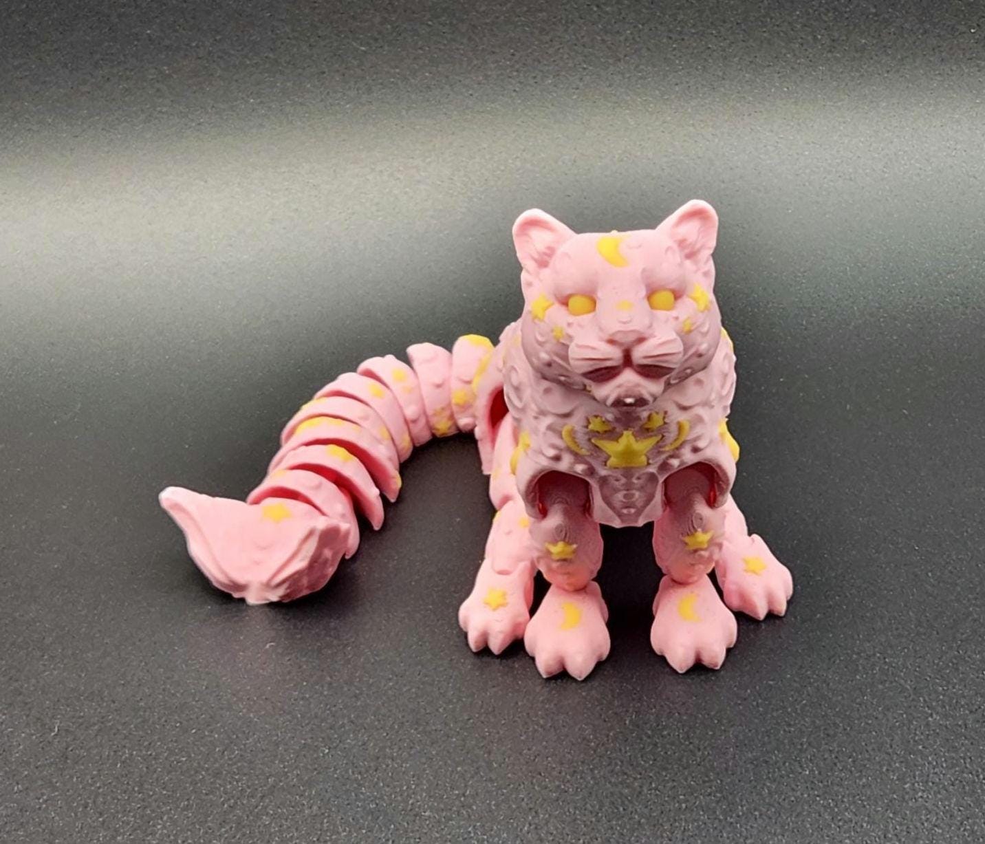 Pink star and moon fidget panther toy with yellow celestial designs on a black background