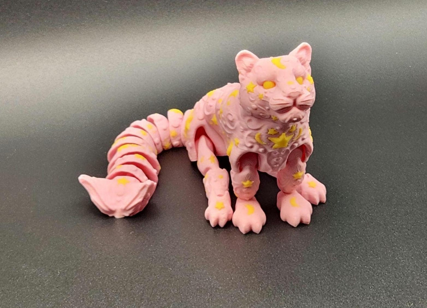 Pink star and moon fidget panther toy with yellow star and moon patterns on a black surface