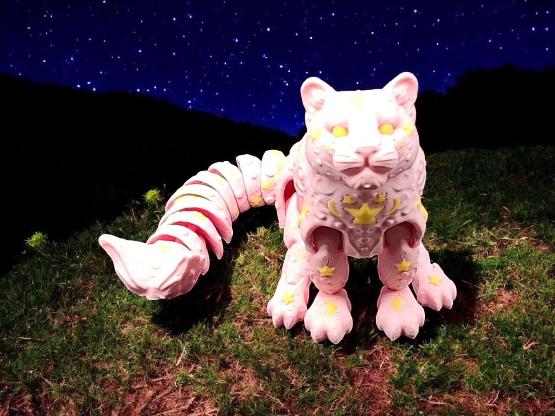 White star and moon fidget panther toy with yellow stars and crescent moons on grass under a starry night sky