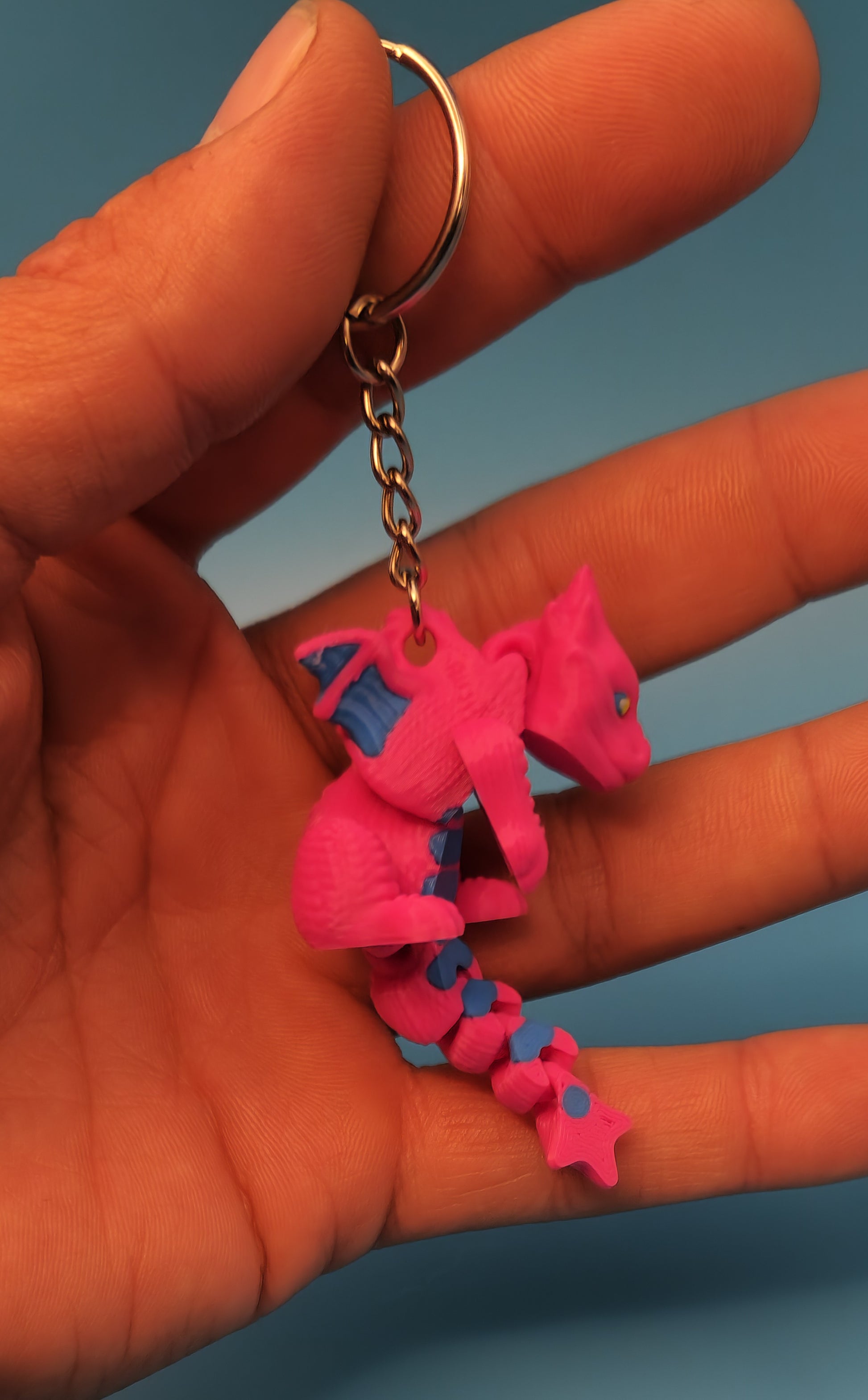 Hand holding a pink and blue 3D printed dragon keychain with detailed wings and tail