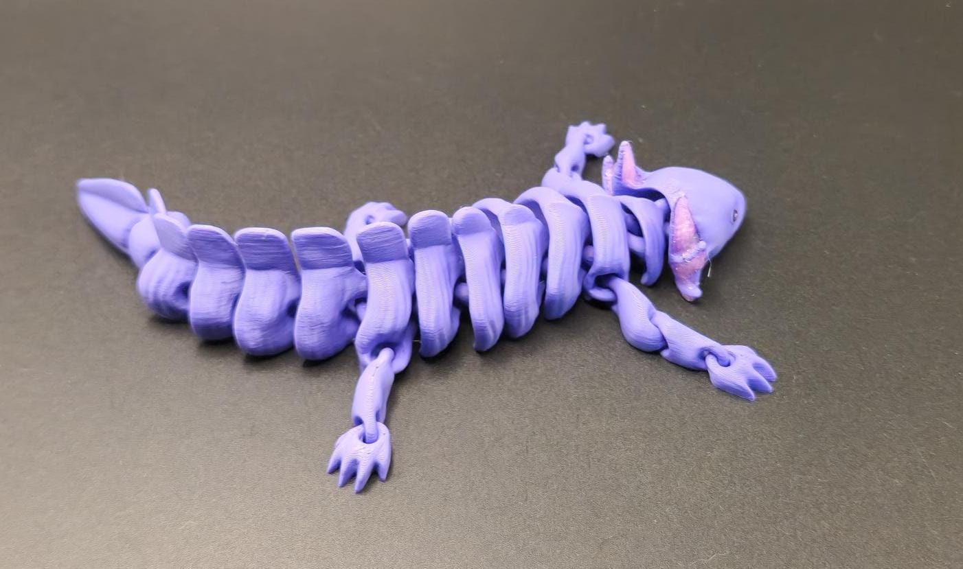 Purple wiggly axolotl figurine with articulated segmented body on gray surface